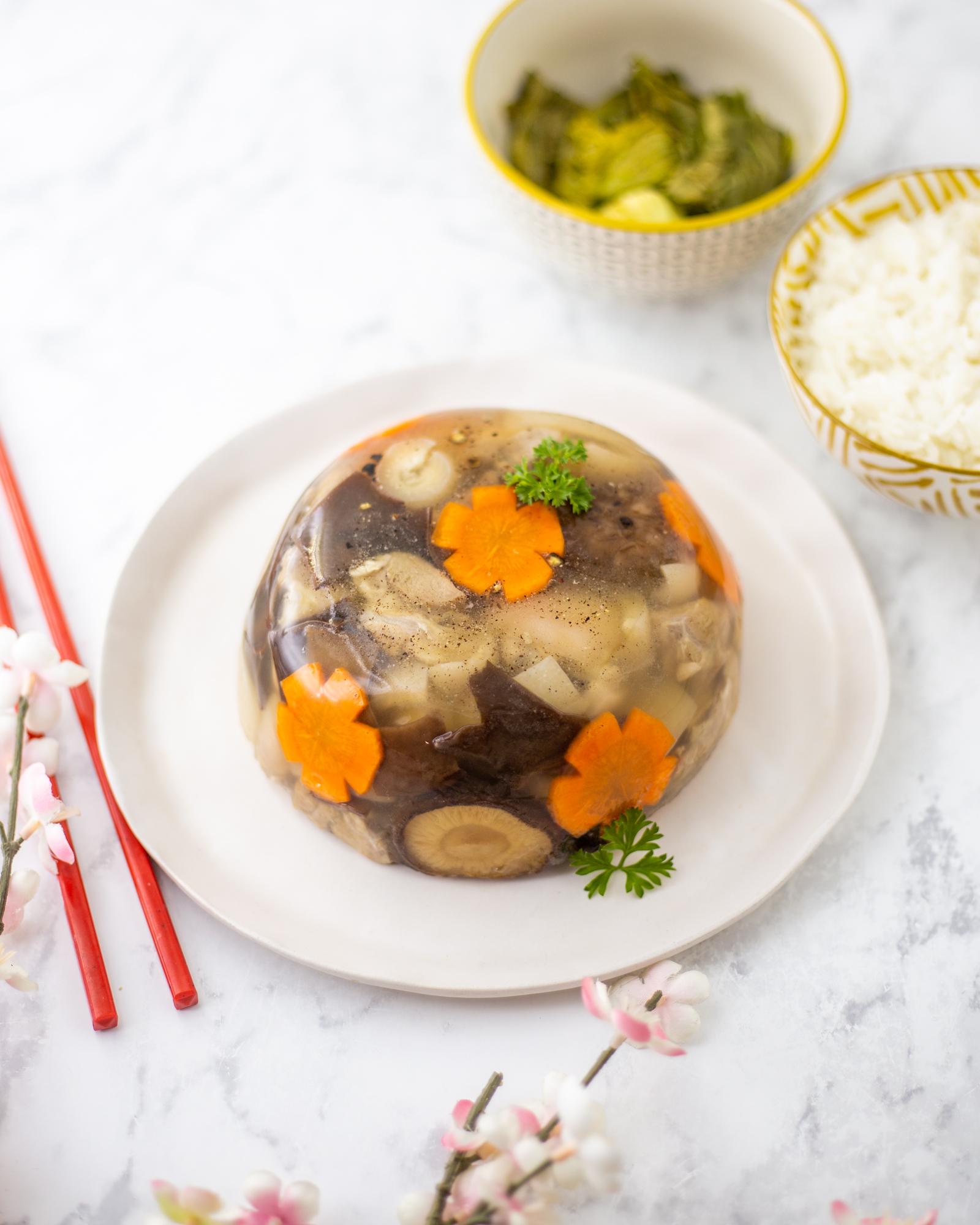 Pork aspic (meat jelly) on a white plate. In the aspic, you can see pieces of pork, mushrooms, and decorative pieces of carrots cut into flowers.